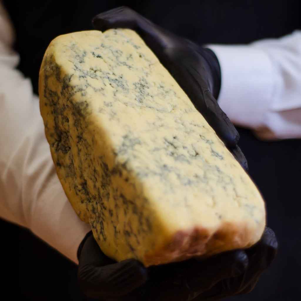 Why The Cheeseroom? Find the top quality blue cheese in Dubai. This image contains the visuals of blue cheese held in gloved hands, highlighting its natural rind and marbled interior.